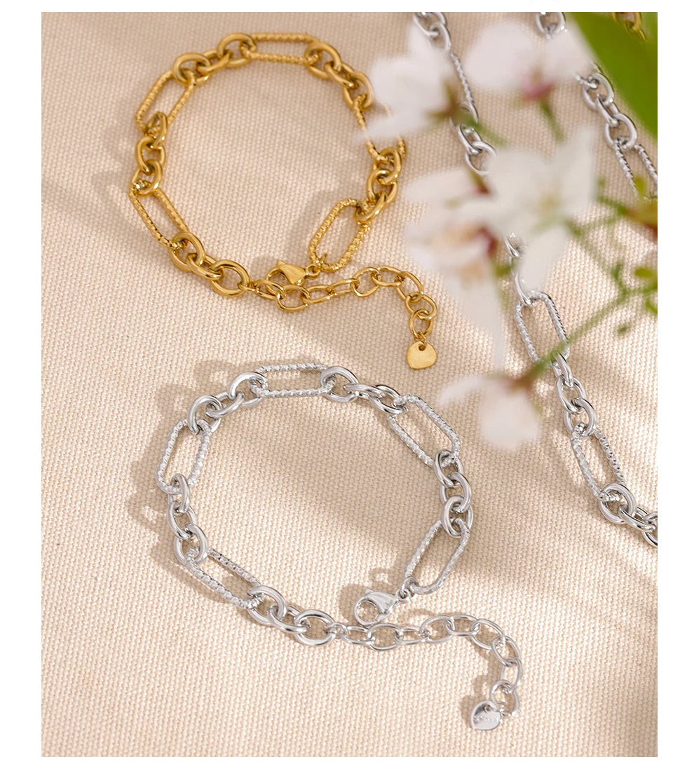 Two chain bracelets, one gold and one silver, on a beige surface with a floral background.
